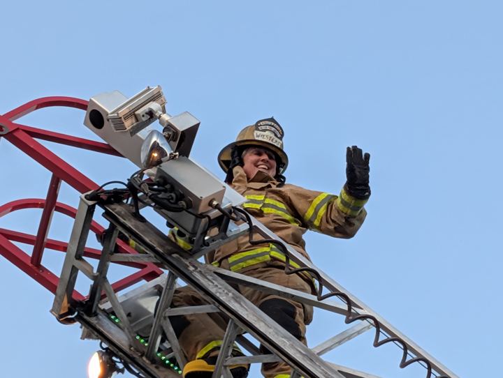 Firefighter waving from the top of a ladder truck