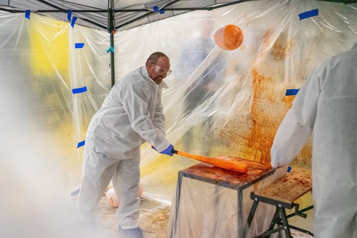 Student in a protective suit creating blood-spatter patterns in the forensics tent